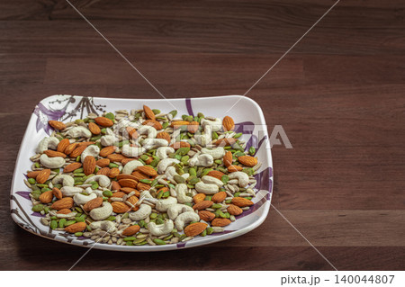 Variety of nuts in a plate on wooden tabletop background. Sources of protein and fat for vegans Variety of nuts in a plate on wooden tabletop background. Sources of protein and fat for vegans 140044807