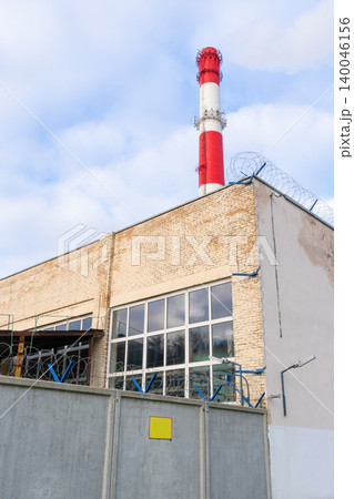 Factory chimney under bright daytime. Clear sky highlights towering chimney beside factory windows 140046156