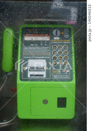 雨の日のガラスの水滴越しに佇む緑色の公衆電話。災害時のインフラやノスタルジーを表現する背景素材 雨の日のガラスの水滴越しに佇む緑色の公衆電話。災害時のインフラやノスタルジーを表現する背景素材 140046818