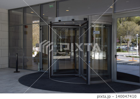 A sleek, modern glass revolving door is prominently featured at the entrance of a commercial building, surrounded by large glass panels and a clean, minimalistic interior design 140047410