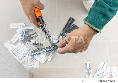 Drywall worker cutting metal profile with tin snips during suspended ceiling installation, hands close up 140047428