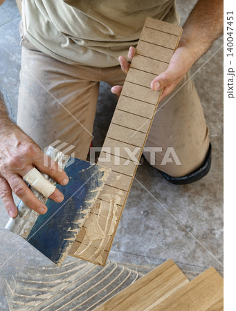 Construction worker applying adhesive on parquet planks during flooring installation in apartment Construction worker applying adhesive on parquet planks during flooring installation in apartment 140047451