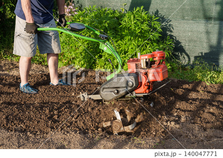 Man using motor cultivator to prepare soil in garden 140047771