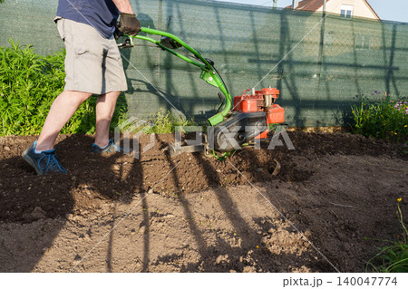 Man using motor cultivator to prepare soil in garden 140047774
