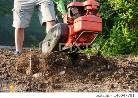 Man using motor cultivator to loosen soil in garden close up Man using motor cultivator to loosen soil in garden close up 140047781