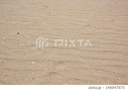 Close-up view of a sandy beach featuring gentle ripples in the sand and scattered small shells, creating a natural texture and pattern under bright sunlight Close-up view of a sandy beach featuring gentle ripples in the sand and scattered small shells, creating a natural texture and pattern under bright sunlight 140047875