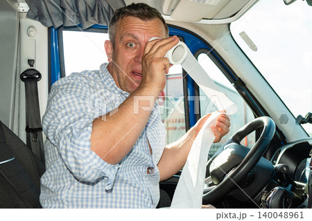 Sad emotional male driver crying and wiping tears with paper roll in cabin. Sad emotional male driver crying and wiping tears with paper roll in cabin. 140048961