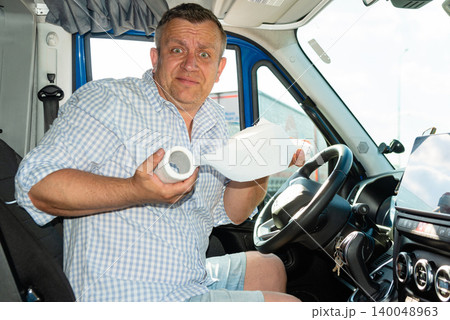 Confused male driver holding a white toilet paper roll inside vehicle cabin. 140048963