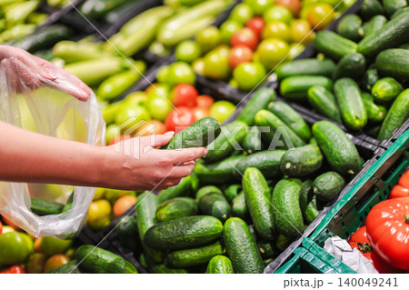 Woman selecting fresh cucumber in supermarket vegetable department Woman selecting fresh cucumber in supermarket vegetable department 140049241