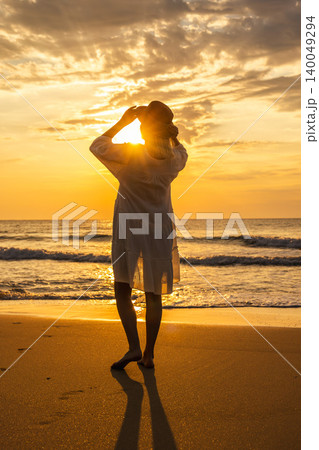Middle aged woman on beach at sunrise adjusting hat, peaceful freedom travel lifestyle by sea Middle aged woman on beach at sunrise adjusting hat, peaceful freedom travel lifestyle by sea 140049294