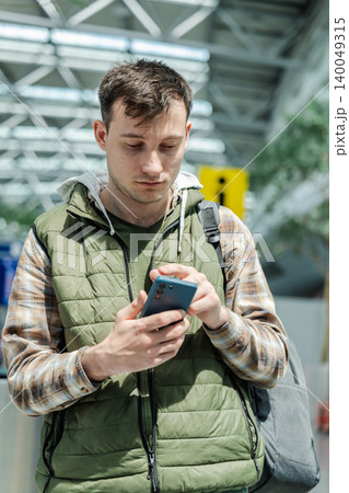 Young male traveler using smartphone while standing in modern airport departure area Young male traveler using smartphone while standing in modern airport departure area 140049315