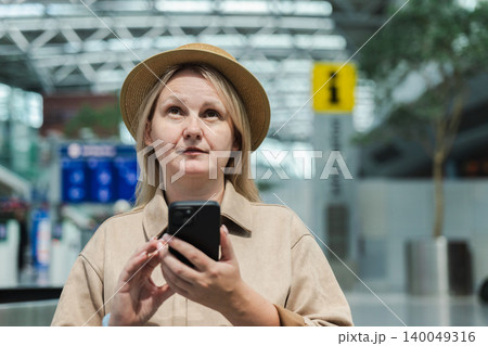 Middle aged woman using smartphone while waiting inside modern airport terminal Middle aged woman using smartphone while waiting inside modern airport terminal 140049316