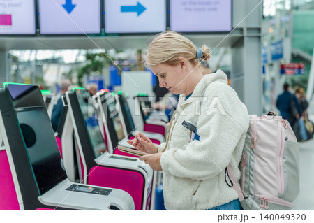 Woman using self check in kiosk with smartphone at modern airport terminal 140049320