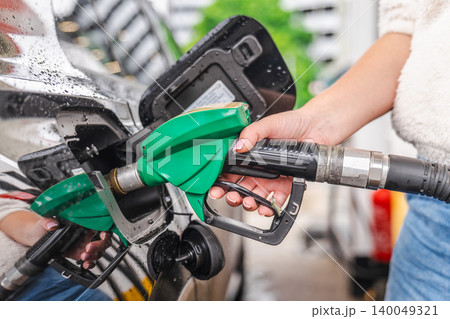 Closeup of woman hand holding fuel nozzle while refueling car at gas station in rainy weather 140049321