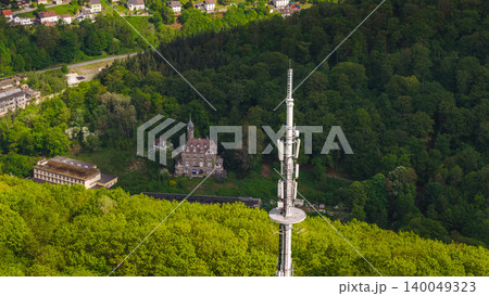 Aerial view of modern communication tower above green forest with historic building and residential area in Germany during sunny spring day 140049323