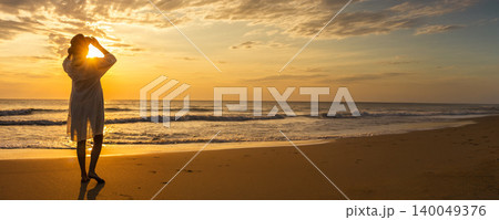 Young woman in white dress enjoying peaceful sunset walk along tropical beach Young woman in white dress enjoying peaceful sunset walk along tropical beach 140049376