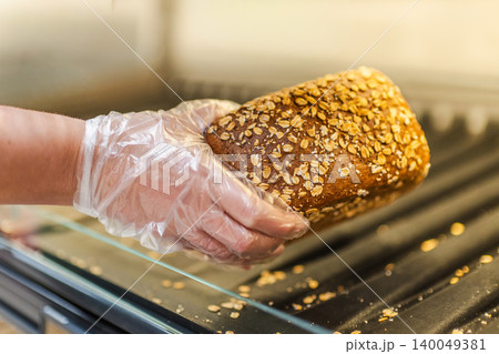 Hand in disposable glove holding fresh oat bread loaf in bakery section of supermarket 140049381