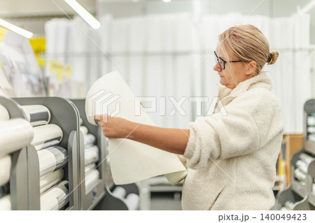 Woman choosing wallpaper sample in home improvement and decor store Woman choosing wallpaper sample in home improvement and decor store 140049423