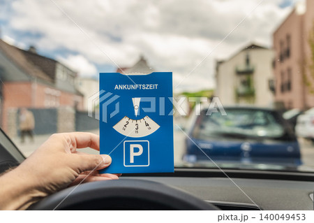 Driver holding German parking disc with word Ankunftszeit meaning arrival time inside car before parking in European city street Driver holding German parking disc with word Ankunftszeit meaning arrival time inside car before parking in European city street 140049453