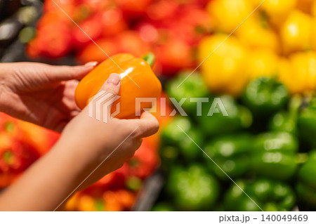 Woman hands holding fresh orange bell pepper in supermarket produce section, colorful vegetables background for healthy grocery shopping concept 140049469