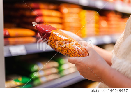 Woman choosing packaged red lentils in supermarket aisle, customer holding dry legumes product while shopping for healthy grocery ingredients Woman choosing packaged red lentils in supermarket aisle, customer holding dry legumes product while shopping for healthy grocery ingredients 140049477