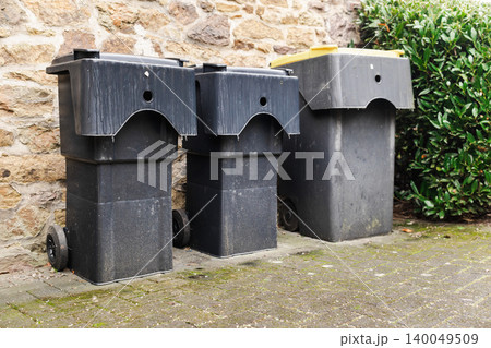 Garbage and recycling bins standing near stone wall in quiet German suburban residential area 140049509