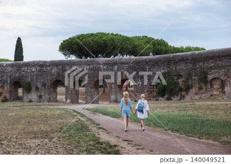 Mother and teenage daughter holding hands walking toward ancient Roman aqueduct arches in Parco degli Acquedotti Rome enjoying travel in Italy Mother and teenage daughter holding hands walking toward ancient Roman aqueduct arches in Parco degli Acquedotti Rome enjoying travel in Italy 140049521
