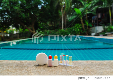 Pool water testing kit and chlorine tablet with reagent bottles on stone edge, clean blue swimming pool background Pool water testing kit and chlorine tablet with reagent bottles on stone edge, clean blue swimming pool background 140049577