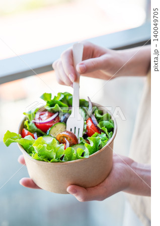 A woman holds a healthy vegetable salad in an eco-friendly takeaway bowl. A woman holds a healthy vegetable salad in an eco-friendly takeaway bowl. 140049705