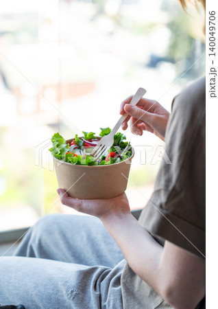 A woman holds a healthy vegetable salad in an eco-friendly takeaway bowl. A woman holds a healthy vegetable salad in an eco-friendly takeaway bowl. 140049706