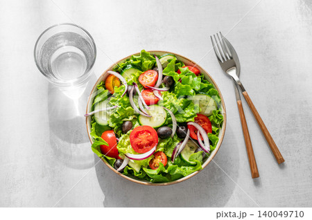 A fresh salad of tomatoes, cucumbers, lettuce, red onions, and olives on a light background A fresh salad of tomatoes, cucumbers, lettuce, red onions, and olives on a light background 140049710