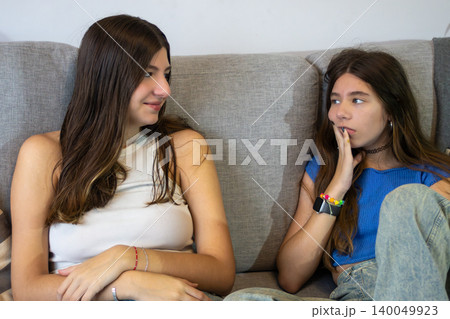 Two gen z friends relaxing on a sofa, sharing an intimate moment, one listening intently while the other looks contemplative, embodying teenage leisure and sisterhood Two gen z friends relaxing on a sofa, sharing an intimate moment, one listening intently while the other looks contemplative, embodying teenage leisure and sisterhood 140049923
