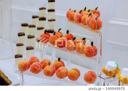 Fruit shaped sweets are arranged on shelves, surrounded by layered desserts at wedding event Fruit shaped sweets are arranged on shelves, surrounded by layered desserts at wedding event 140049970