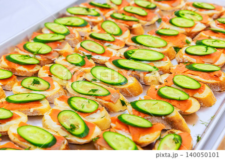 Large tray displays many pieces of bread topped with cream cheese, smoked salmon, cucumber, ready for guests. Large tray displays many pieces of bread topped with cream cheese, smoked salmon, cucumber, ready for guests. 140050101