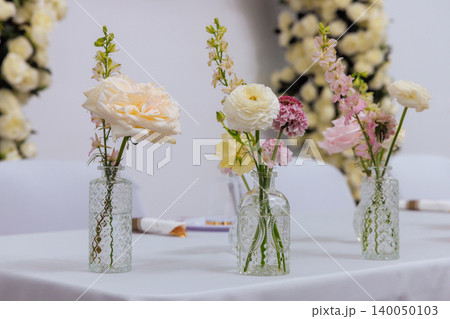 Vases filled with white pink flowers sit on wedding table at decorated event space with floral backdrop. Vases filled with white pink flowers sit on wedding table at decorated event space with floral backdrop. 140050103