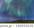 Vibrant aurora borealis dances across the starry night sky above a grassy hill 140050226