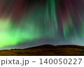 Vibrant green and red aurora borealis dances across a starry night sky over a hill 140050227