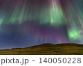Vibrant aurora borealis dances across the night sky over rolling hills 140050228