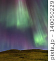 Vibrant aurora borealis dances across a starry night sky over rolling hills 140050229