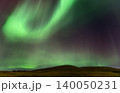 Vibrant green aurora borealis dances across a starry night sky over rolling hills 140050231