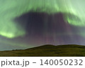 Vibrant green and purple aurora borealis dances across a starry night sky 140050232