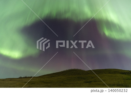 Vibrant green and purple aurora borealis dances across a starry night sky Vibrant green and purple aurora borealis dances across a starry night sky 140050232