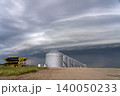 Agricultural grain silos stand under a dramatic, stormy sky with a farm implement nearby 140050233