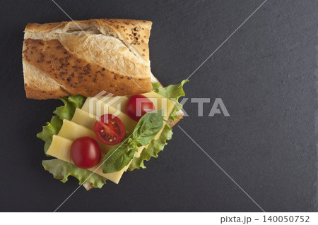 Sandwich with cheese, tomatoes, and greens on a granite floor. 140050752