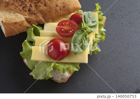 Sandwich with cheese, tomatoes, and greens on a granite floor. 140050753