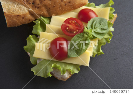 Sandwich with cheese, tomatoes, and greens on a granite floor. 140050754