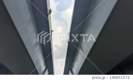 Symmetrical low angle perspective captures massive twin concrete overpass structures, framing a bright cloudy sky. The heavy brutalist urban architecture creates strong parallel lines, gritty 140051572