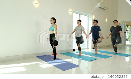 Yoga instructor leading group in tree pose balance exercise in bright studio, focusing on stability, concentration and body alignment to improve core strength and mindfulness during class practice Yoga instructor leading group in tree pose balance exercise in bright studio, focusing on stability, concentration and body alignment to improve core strength and mindfulness during class practice 140052885