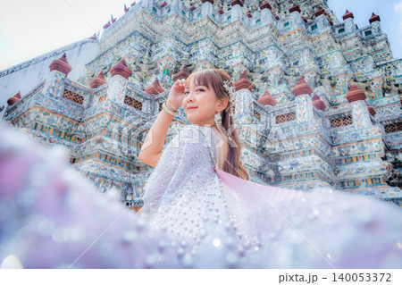 Close up of a young woman wearing traditional Thai dress with accessories standing at Wat Arun, a popular place for tourists around the world. Bangkok Thailand Close up of a young woman wearing traditional Thai dress with accessories standing at Wat Arun, a popular place for tourists around the world. Bangkok Thailand 140053372