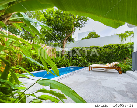 Pool chairs and beautiful blue water with green tree in the background. 140053412